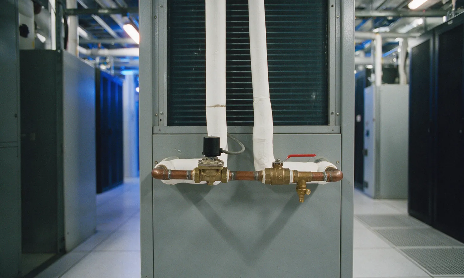 A pre-assembled brass valve assembly with a small actuator, a red-lever ball valve and a drain cock on the chilled-water connections of an air handling unit