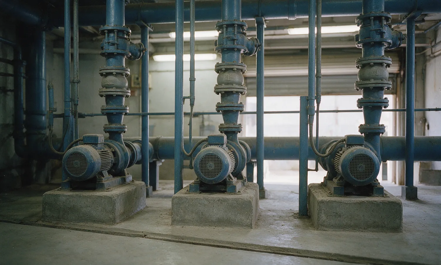 Three end-suction pumps on concrete plinths, each discharge pipe rising through flanged valves